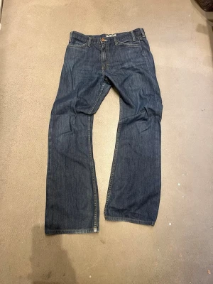 Mörkblå raka jeans - Klassiska mörkblå jeans med bootcut passform och fem fickor. Jeansen har normal midja, knappgylf och kontrastsömmar. Tillverkade i denim med en tidlös look som passar till det mesta. Perfekta för dig som gillar enkel och stilren stil. W29 L32