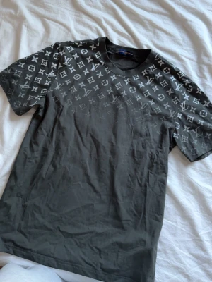 Svart  t-shirt med monogram - Snygg svart t-shirt med klassiskt monogrammönster i vitt över axlar och bröst. T-shirten har rund halsringning och korta ärmar. Tillverkad i mjuk bomull för en bekväm känsla och stilren look.