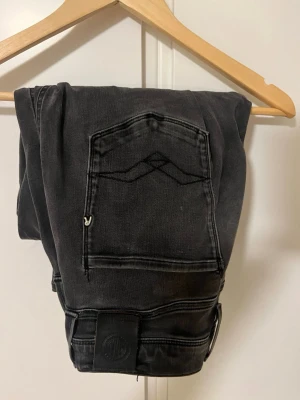 Svarta jeans från Wrangler - Säljer ett par svarta jeans från Wrangler med klassisk femficksdesign och diskret broderad detalj på bakfickan. Jeansen har raka ben och är tillverkade i slitstark denim. Perfekta för en avslappnad och cool stil.