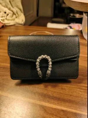 Dionysus Super Mini  - Elegant black pebbled leather Dionysus Super Mini with statement crystal horsebit clasp and gunmetal chain strap. A timeless design that transitions effortlessly from day to night. ✨ Crystal horsebit detail ✨ Gunmetal chain strap ✨ Multiple interior compartments ✨ Compact yet surprisingly spacious ✨ Perfect for everyday wear, dinners, events, and nights out  📦 Original box included Bought preloved, can send the digital receipt I received.