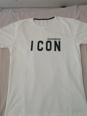 Vit ICON t-shirt från Dsquared2 - Snygg vit t-shirt från Dsquared2 med stor svart 'ICON'-text och logga på bröstet. Klassisk rund hals och korta ärmar. Tillverkad i mjuk bomull som känns skön mot huden. Perfekt för dig som gillar stilrena och trendiga plagg.