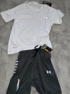 Under Armour träningsset t-shirt & shorts - Snyggt träningsset från Under Armour med en vit t-shirt i lätt och ventilerande material samt mörk grå shorts.