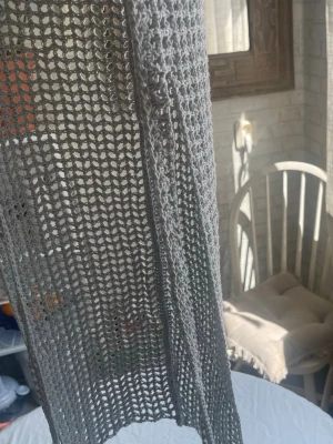 Grå virkad durag - Snygg grå durag i virkad design med öppet nätmönster. Tillverkad i ett mjukt garn som ger en luftig och trendig look. Perfekt accessoar för att lyfta din outfit och skydda håret. Två band för att kunna knyta i valfri stil.