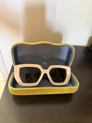 Vita fyrkantiga solglasögon Gucci - Säljer ett par riktigt snygga solglasögon från Gucci med vit, fyrkantig båge och svarta glas. Bågarna är i kraftig plast och har svarta skalmar. Kommer med originalfodral i gul sammet. Perfekt accessoar för dig som vill sticka ut. Dessa är äkta dessutom