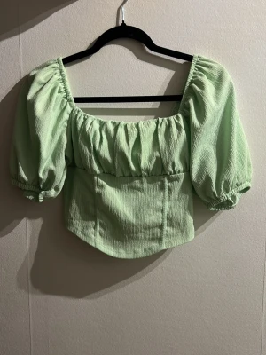 Grön puffärm topp från Gina Tricot - Trendig ljusgrön topp från Gina Tricot med puffiga korta ärmar och smockad struktur. Toppen har en fyrkantig ringning och sitter snyggt figurnära i midjan. Perfekt för dig som vill sticka ut med en färgklick i garderoben💚 Använd fåtal gånger! (Sista bilden är lånad) 