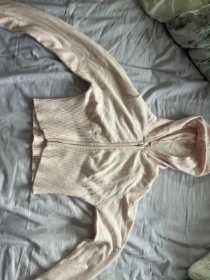 Ljusrosa croppad hoodie med dragkedja - Säljer en ljusrosa croppad hoodie med dragkedja framtill. Hoodien har ribbad midja och långa ärmar. Perfekt för en chill och avslappnad stil. Materialet känns mjukt och bekvämt, troligen bomull eller bomullsblandning. Inga synliga loggor eller märken.