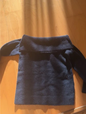 Mörkblå off shoulder stickad tröja - Snygg mörkblå stickad tröja från Gina Tricot med bred off shoulder-krage. Tröjan har lång ärm och är gjord i ett mjukt, fluffigt material som känns riktigt cozy. Perfekt för dig som vill ha en trendig och bekväm look.
