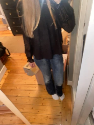 Svart blus med volang från Gina Tricot - Säljer en svart blus från Gina Tricot med transparenta, långärmade ärmar och volangdetaljer vid halsen. Blusen har en luftig passform och är tillverkad i ett tunt, lätt material som ger en elegant look.