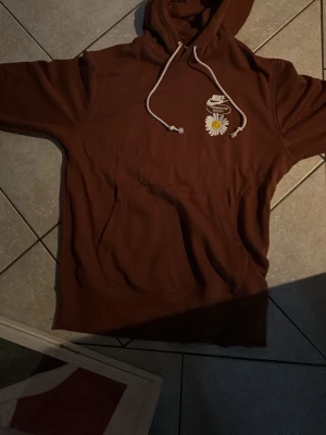 Brun hoodie från Nike med blomma  - Säljer en brun hoodie från Nike med vit dragskedja och en broderad prästkrage och Nike-logga på bröstet Hoodie är helt ny kostar 999kr ny men säljer den billigare för behöver pengarna . Hoodien har en klassisk känguruficka och mjukt material som känns skönt mot huden. Perfekt för dig som gillar streetwear och snygga detaljer. 