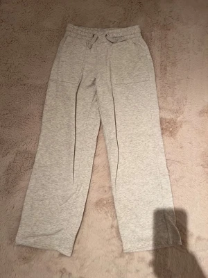 Ljusgrå mjukisbyxor med raka ben - Säljer ett par ljusgrå mjukisbyxor med raka ben och resår i midjan samt dragsko. Byxorna har stora fickor fram och bak, och är tillverkade i mjukt sweatshirtmaterial. Perfekta för chill dagar eller när du vill vara extra bekväm.