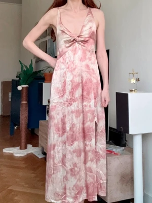 Rosa vit mönstrad klänning - Säljer en fantastiskt fin långklänning från Zara i mjukt, glansigt material med mönster i rosa och vitt. Klänningen har smala axelband, v-ringning med twistdetalj framtill och en slits på sidan. Perfekt för sommaren, fester, bröllop och andra tillställningar. Har en dragkedja på sidan. Passar storlek XS och S. Ej genomskinlig. Banden är inte justerbara. Nyskick.