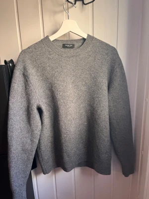 Grå stickad tröja Massimo Dutti - Mysig grå stickad tröja från Massimo Dutti med rund halsringning och ribbade muddar vid ärmslut och nederkant. Klassisk och enkel design som passar perfekt till lager-på-lager. Materialet ser ut att vara mjukt och värmande ullblandning. Tröjan är L men sitter som en S/M