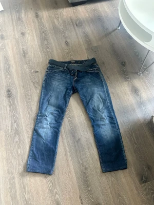 Blå jeans från Replay  - Snygga blå jeans från Replay i klassisk rak modell. Jeansen har slitningar och tvättade detaljer för en cool look. Tillverkade i bomull med en skön passform som passar till många stilar. Schysst pris vid snabb affär🙌
