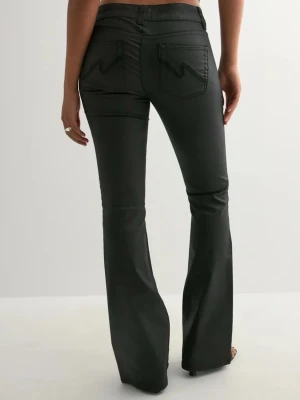Svarta bootcut jeans/byxor  - Snygga svarta bootcut jeans från melly med låg midja  och pressveck framtill. Jeansen har klassiska fem fickor och dubbla silverknappar i midjan. Materialet har en lätt glansig finish som ger en modern touch.