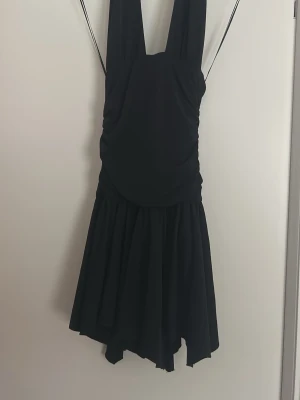 Svart klänning från Bershka - Snygg svart klänning från Bershka med breda axelband och volangig kjol. Klänningen har en figurnära överdel och ett flowy fall nedtill. Perfekt för dig som gillar en stilren och trendig look.