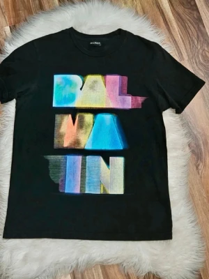 Svart Balmain t-shirt med färgglatt tryck - Säljer en svart t-shirt från Balmain med stort, färgglatt tryck framtill i blått, gult, rosa och grönt. T-shirten har rund hals och korta ärmar. Perfekt för dig som vill sticka ut med en statement tee. I fint skick använd max 10 gånger. 