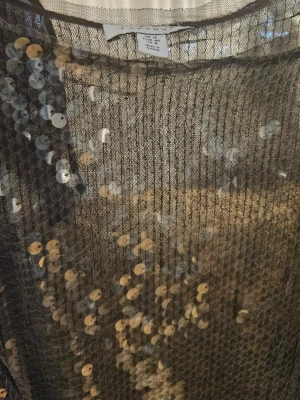 Glittrig långklänning med paljetter - Säljer en glittrig långklänning från Topshop med silverfärgade paljetter över hela klänningen. Klänningen har en rak och elegant form, är ärmlös och passar perfekt för dig som vill sticka ut. Materialet är polyester och klänningen har en slits på sidan.