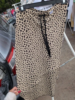House of lola Beige leopardmönstrad långkjol - Snygg beige långkjol med svart leopardmönster och svart snörning i midjan. Kjolen har en avslappnad passform och är perfekt för dig som vill sticka ut lite extra. Tillverkad i mjukt material som känns skönt mot huden. Lite stor i storlek. 
