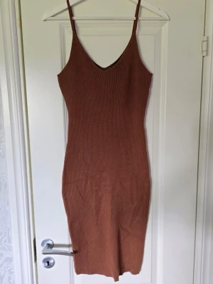 Brun ribbad klänning från SHEIN - Säljer en brun ribbad klänning från SHEIN med smala axelband och v-ringning. Klänningen är figurnära och har en enkel, stilren design som passar perfekt till sommaren. Materialet är stretchigt och bekvämt.