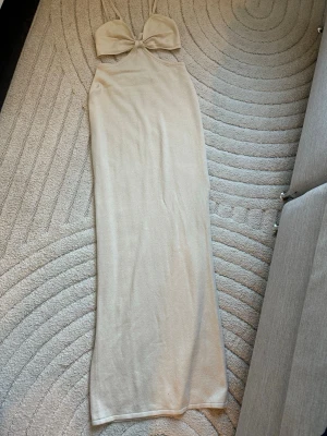Beige långklänning med cut out - Trendig beige långklänning med smala axelband och snygg cut out-detalj under bysten. Klänningen har en figurnära passform och är tillverkad i ett mjukt, stickat material som ger en lyxig känsla. Perfekt för dig som vill ha en stilren och modern look.