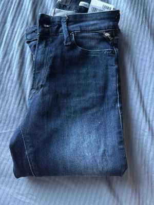 Mörkblå jeans från Replay - Snygga mörkblå jeans från Replay med klassisk femficksmodell och diskreta slitningar framtill. Jeansen har en smal passform och är tillverkade i stretchigt denimtyg för extra komfort. Perfekta för dig som gillar en stilren och modern look.