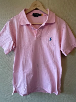 Rosa pikétröja från Polo Ralph Lauren - Klassisk rosa pikétröja från Polo Ralph Lauren med blå broderad logga på bröstet.  Den e i bra skick och storleken är S 