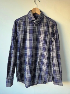 Blårutig skjorta från Tommy Hilfiger - Klassisk blårutig skjorta från Tommy Hilfiger med lång ärm och knappstängning framtill. Skjortan har en bröstficka med diskret logga och är tillverkad i mjuk bomull. Perfekt för en avslappnad men ändå stilren look.