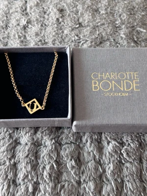 Guldarmband Charlotte Bonde - Snyggt guldhalsband från Charlotte Bonde med en kedja i guldfärg och ett fyrkantigt hänge med ett stilrent U-inspirerat motiv. Kommer i original ask och har en modern, minimalistisk design som passar perfekt till din outfit. made from Sterling Silver or Gold plated Sterling Silver.