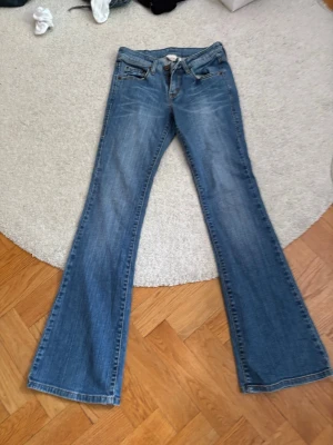 Blå bootcut jeans med slitningar - Säljer ett par blå bootcut jeans med snygga slitningar och klassisk femficksmodell. Jeansen har normalhög midja och är tillverkade i denim med lätt stretch.