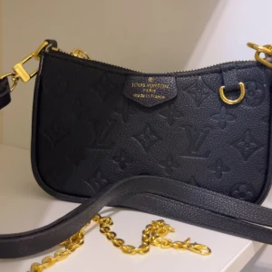 Svart Louis Vuitton axelväska i skinn - Säljer en svart axelväska från Louis Vuitton med klassiskt monogrammönster i präglat skinn. Väskan har guldfärgade metalldetaljer, dragkedja och både axelrem i skinn och kedja. Perfekt storlek för det viktigaste och riktigt snygg design.