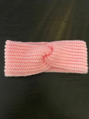 Rosa virkat pannband - Säljer ett mjukt virkat pannband i ljusrosa färg. Pannbandet har en twistad detalj framtill och är gjort i ett garn som känns varmt och skönt. Perfekt accessoar för kyliga dagar.