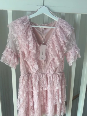 Rosa spetsklänning med volanger - Sommarklänning från gina tricot 14+, helt ny och aldrig använd!! klänningen är mindre i verkligheten, har själv XS-S egentligen. Kontakta vid funderingar💗🌟