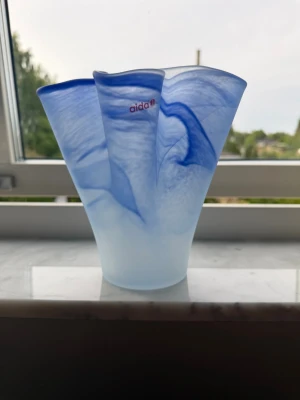 Blåvit vågig glasvas från Aida - Snygg blåvit vas i glas från Aida med vågig och organisk form. Glaset har en mjuk, matt finish och unika blå marmoreringar som ger ett konstnärligt intryck. Perfekt som dekoration eller för blommor och ger ett modernt uttryck till rummet.