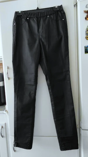 Svarta leggings med jeanslook - Svarta byxor med resår i midjan. Byxorna har fickor fram och bak, samt små nitar som detaljer. Storlek M. Knappt använda.
