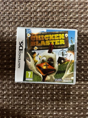 Chicken Blaster till Nintendo DS - Chicken Blaster är ett actionfyllt spel till Nintendo DS där du skjuter galna höns i olika miljöer. Omslaget är färgglatt med en tecknad höna i fokus och spelet är utvecklat av Zushi. Perfekt för dig som gillar humoristiska och snabba spel.