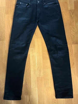 Svarta jeans Dressmann - Snygga svarta jeans från Dressmann. Klassisk femficksmodell med smal passform och normal midja. Jeansen är tillverkade i ett stretchigt material som ger skön komfort och stilren look. Perfekta till både sneakers och boots.