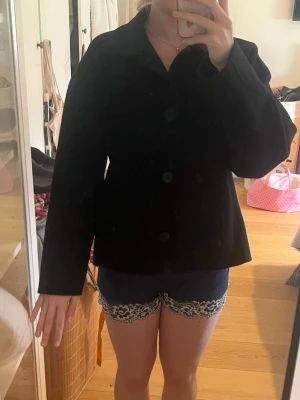 Svart kappa från Lindex XS - Stilren svart kappa från Lindex i storlek XS. Klassisk rak modell med krage och stora knappar framtill. Perfekt för dig som gillar en enkel och tidlös look. Materialet känns mjukt och passar bra till olika outfits.