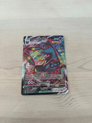 Umbreon VMAX Pokémonkort - Säljer ett Umbreon VMAX Pokémonkort från Sword & Shield-serien. Kortet har färgstark holografisk design med Umbreon i fokus och detaljer i svart, blått och rött. Perfekt för samlare eller Pokémonfans som vill utöka sin kortsamling.