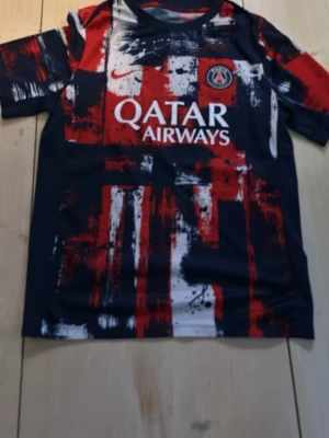 PSG matchtröja med grafiskt mönster - Säljer en Paris Saint-Germain matchtröja från Nike med Qatar Airways-tryck. Tröjan har ett unikt grafiskt mönster i rött, vitt och marinblått. Korta ärmar och rund hals. Perfekt för fotbollsträning eller att bära som supporter.
