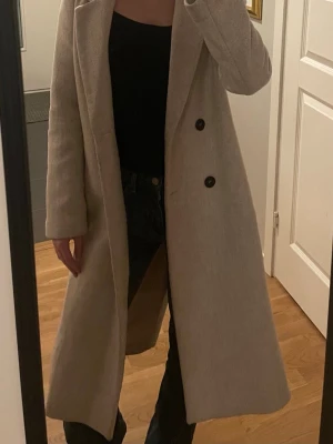 Lång beige kappa  - Lång beige kappa med dubbelkläppning samt skärp