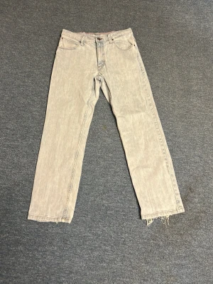 Ljusblå raka jeans från Wrangler - Ljusblåa jeans från Wrangler med rak passform och klassisk femficksdesign. Jeansen har en något tvättad look och råa, fransiga benslut för en avslappnad vibe. Perfekta för dig som gillar en stilren men ändå trendig look.