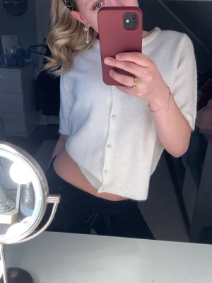 Vit kofta med pärlknappar från Lager 157 - Kort, vit kofta från Lager 157 med rund halsringning och pärlknappar framtill. Koftan har korta ärmar och är stickad i ett mjukt material. Perfekt för lager på lager och enkel att matcha med olika outfits.