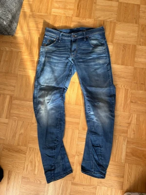 Blå jeans från G-Star RAW - Säljer ett par blå jeans från G-Star RAW med snygga slitningar och tvättade detaljer. Klassisk femficksmodell med raka ben och logotyp på bakfickan. Perfekta för en avslappnad och trendig stil. Materialet är denim i bomull.