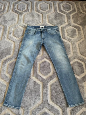 Blå slim fit jeans från Replay - Snygga blå slim fit jeans från Replay med klassisk femficksdesign och diskret slitning på låren. Jeansen har normal midja och raka ben, perfekta till en avslappnad stil. Tillverkade i mjukt denimtyg för skön känsla hela dagen. W34 L32