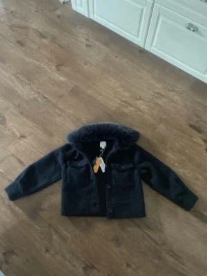 Mörk teddyjacka med pälskrage - Säljer en mörk teddyjacka från Gina Tricot med fluffig pälskrage och två stora bröstfickor med knappar. Jackan har en rak passform och stängs med knappar framtill. Perfekt för dig som vill ha en mysig och trendig look.