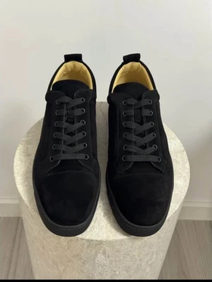 Svarta Louboutin med låg profil - Stilrena svarta Louboutin  i mocka med lågt skaft och svarta snören. Skorna har en klassisk siluett och svart yttersula. Insidan är ljusbeige vilket ger en snygg kontrast. Perfekta för dig som gillar minimalistisk och clean stil.