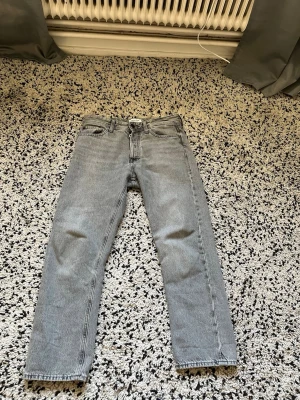 Ljusgrå raka jeans - Säljer ett par ljusgrå jeans med rak passform och klassisk femficksdesign. Jeansen har normal midja och är tillverkade i denim. Perfekta för en avslappnad och trendig look.