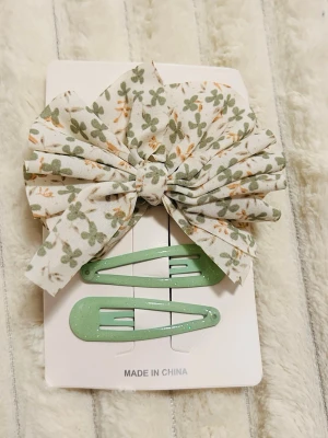 Blommig rosett & mintgröna hårspännen - Säljer ett set med en stor tygrosett i vitt med grönt och orange blommönster samt två mintgröna hårspännen med glitter. Perfekt för att piffa upp frisyren med en söt och trendig touch.