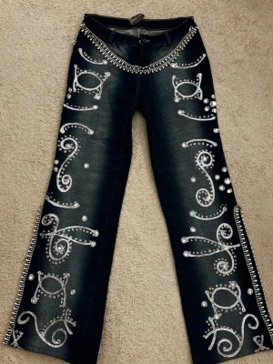 Y2K rhinestone jeans – vintage bling / mcbling style - Unika mörkblå jeans från Dollskill med breda ben, dekorerade med silvriga glittermönster och stora strassdetaljer. Midjan pryds av en rad metallnitar och dragkedjor längs sidorna ger extra edge. Perfekta för dig som vill sticka ut och älskar statement-plagg. (Jätte gamla jeans från 2000-talet) priset kan diskuteras!