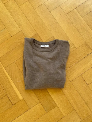 Brun stickad tröja från Replay - Snygg brun stickad tröja från Replay med rund halsringning och diskret logolapp vid nederkanten. Tröjan har en enkel och stilren design med långa ärmar och ribbade muddar. Perfekt för lager på lager och passar till det mesta.